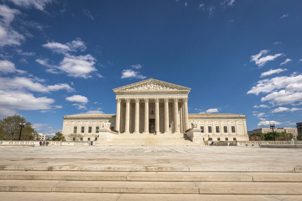 Front view of the United States Supreme Court building on a sunny day with blue sky and clouds.